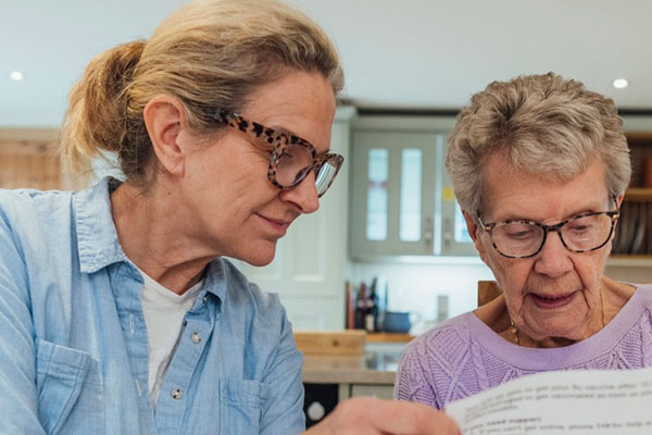 An older woman and her daughter going through paperwork before an aged care assessment.