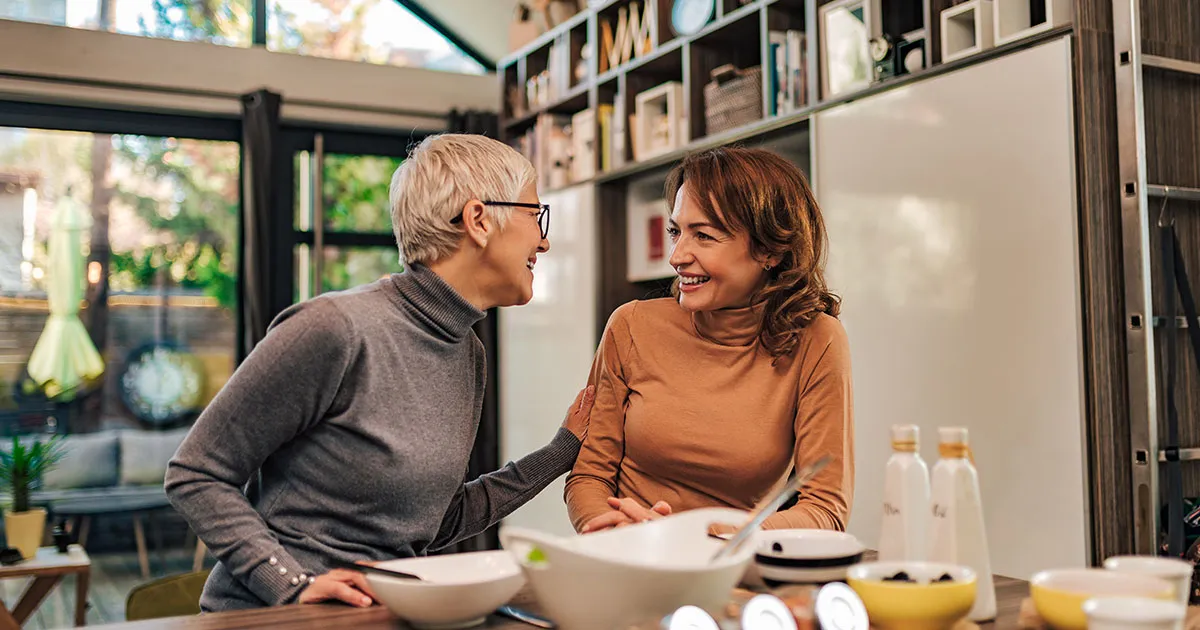 An older woman and her daughter sitting together at the kitchen table with an aged care assessor.