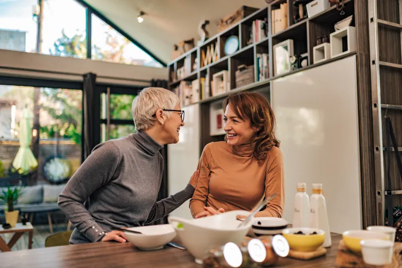 An older woman and her daughter sitting together at the kitchen table with an aged care assessor.