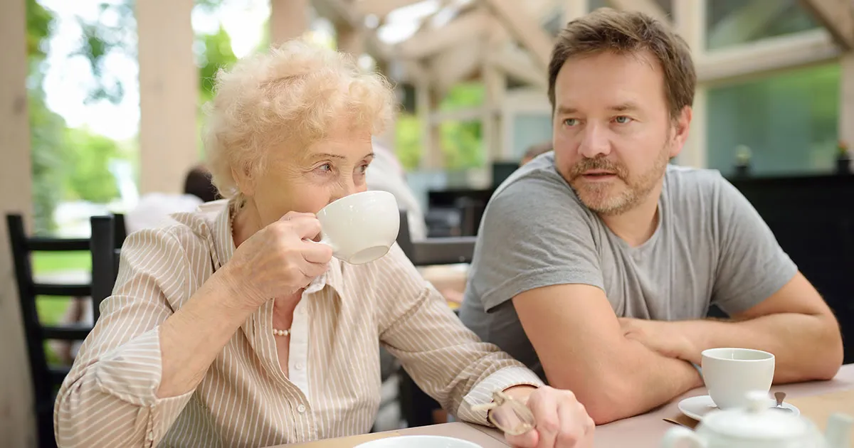 An older woman and her adult son sharing a cup of tea in a bright aged care home lounge