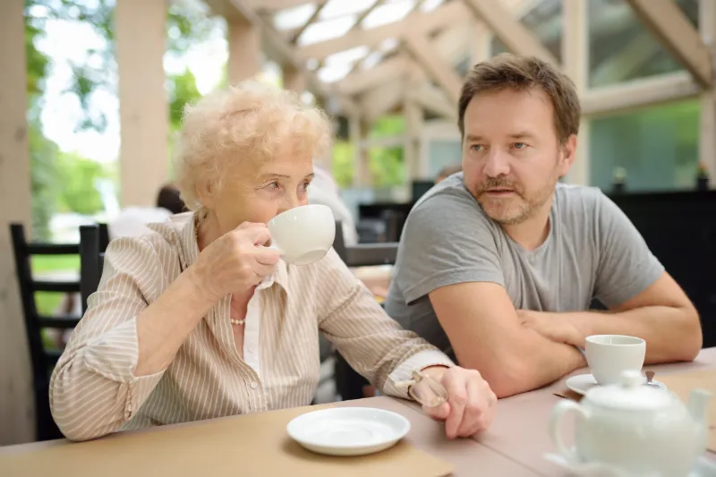 An older woman and her adult son sharing a cup of tea in a bright aged care home lounge